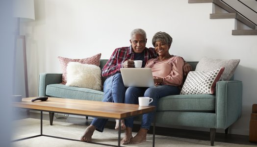 Senior Couple Sitting On Sofa At Home Using Laptop To Shop Online